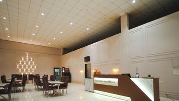 A hotel reception area with a modern design, featuring a reception desk, seating area with chairs and tables, and a decorative light fixture on the ceiling.