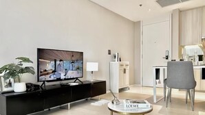 Een moderne woonkamer met een flatscreen televisie, een zwarte entertainmentkast, een ronde salontafel en een grijze stoel.