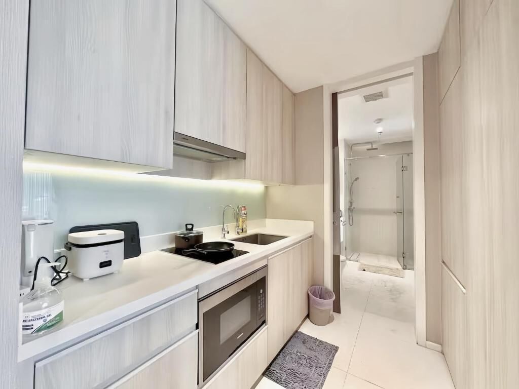 A modern kitchen with a microwave, stove, and sink, leading to a shower area.