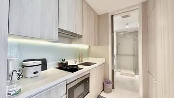 A modern kitchen with a microwave, stove, and sink, leading to a shower area.