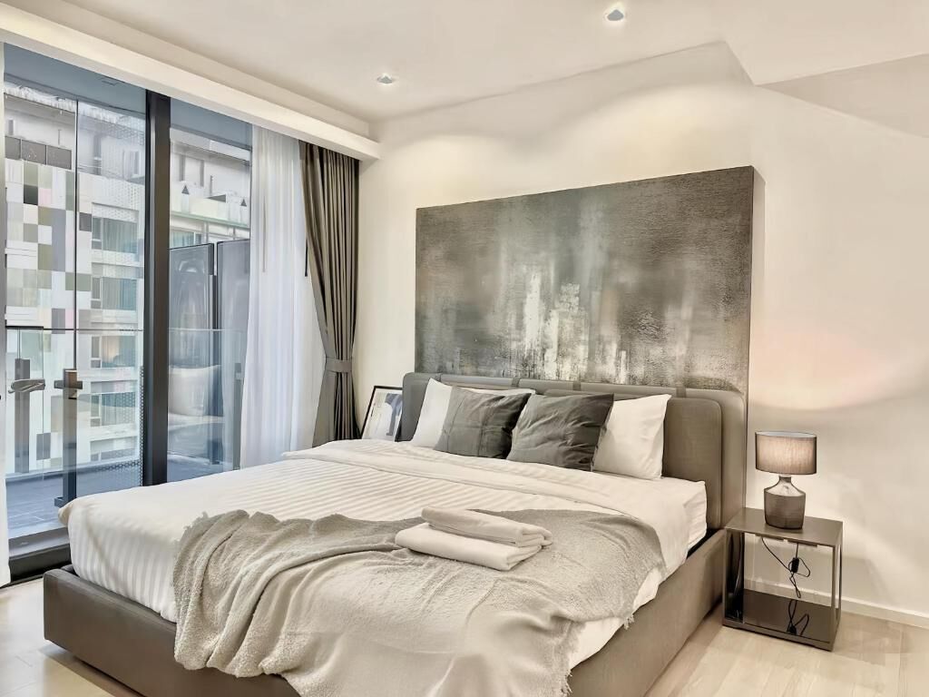A modern bedroom with a large bed, a cityscape view through the window, and a contemporary art piece above the bed.