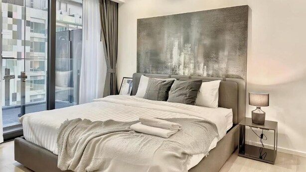 Een moderne slaapkamer met een groot bed, een stadsgezicht door het raam en een eigentijds kunstwerk erboven.