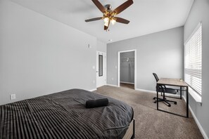 Une chambre à coucher comprenant un lit, un bureau, une chaise, un ventilateur de plafond et un placard.