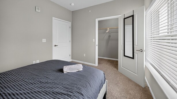Un dormitorio con cama, una puerta, armario y ventana con persianas.