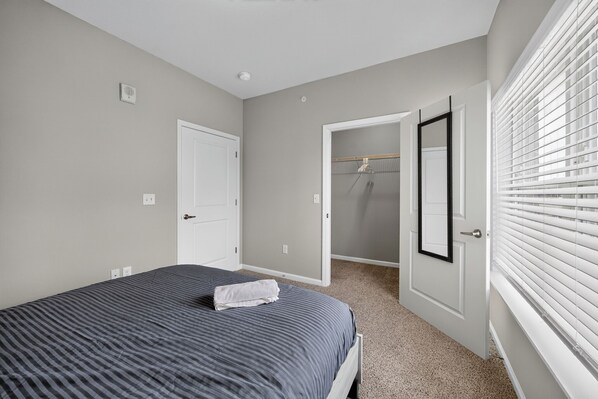 A bedroom with a bed, a door, a closet, and a window with blinds.