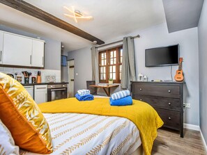 A bedroom with a bed, a television, a guitar, and a kitchen area. - Waterfront Stay for Two (Whitby)
