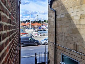 A view through a window of a building with a brick exterior, overlooking a marina with boats and a street with parked cars. - Waterfront Stay for Two (Whitby)