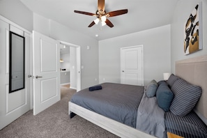A bedroom with a bed, a ceiling fan, and a door leading to another room.