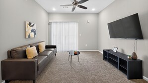 A living room with a sofa, a coffee table, a TV, and a ceiling fan. - Whitewing Flats Retreat (Princeton)