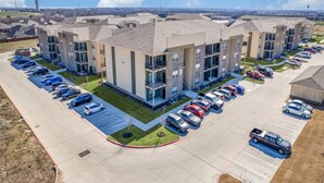 A multi-story parking structure with a row of cars parked in front of a building with balconies. - Whitewing Flats Retreat (Princeton)