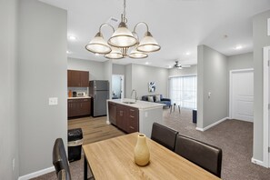 A modern kitchen with a central island, a dining area with a table and chairs, and a living area with a sofa and a large window. - Whitewing Flats Retreat (Princeton)