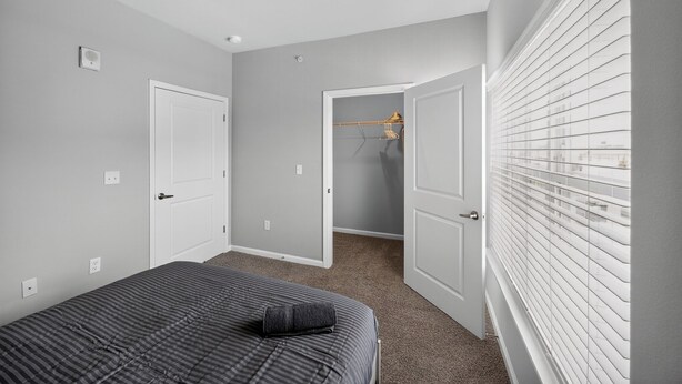 A bedroom with a bed, two doors, and a closet with a hanging rack. - Whitewing Flats Retreat (Princeton)