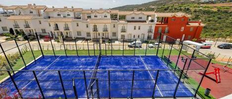 A sports court with a blue surface, surrounded by a metal fence, and buildings in the background.