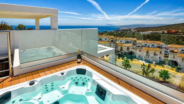 En balkon med jacuzzi og gelænder af glas med udsigt over en kystby.