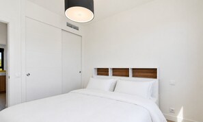 Ein Schlafzimmer mit einem Bett, weißen Wänden, einem hölzernen Kopfteil und einer Deckenleuchte.