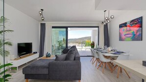 En moderne stue med en grå sofa, et fladskærms-tv og et spiseområde med et bord dækket til fire personer.