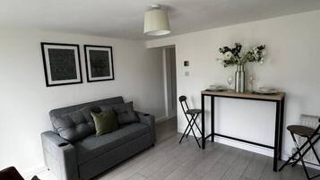 A modern living room with a grey sofa, a wooden coffee table, and a dining area with a table and chairs.