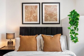 Een hotelkamer met een bed, twee kunstwerken in lijsten, een bedlamp en een groene plant.
