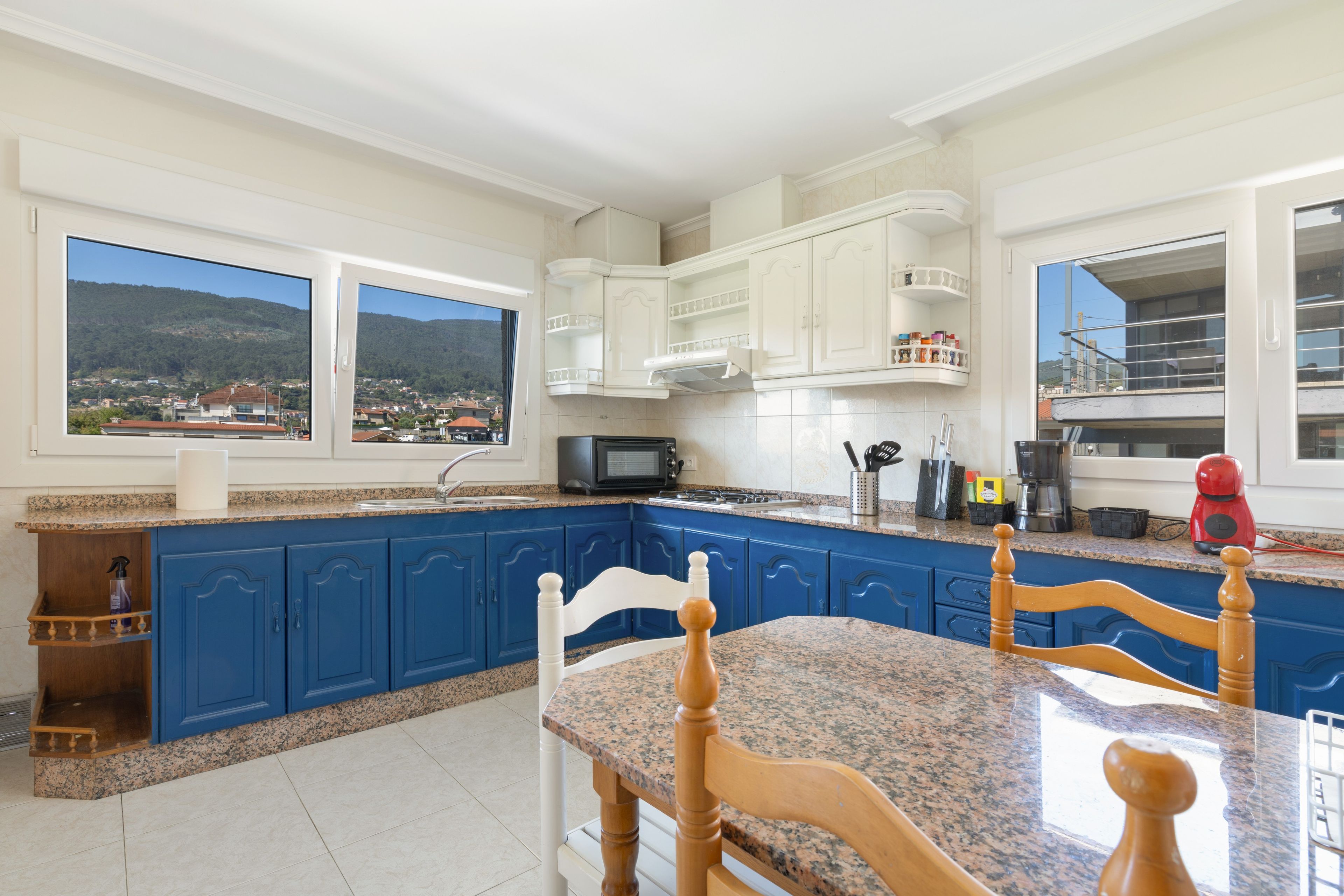 Eine Küche mit blauen Schränken, einer Granit-Arbeitsplatte und Blick auf eine gebirgige Landschaft durch die Fenster.