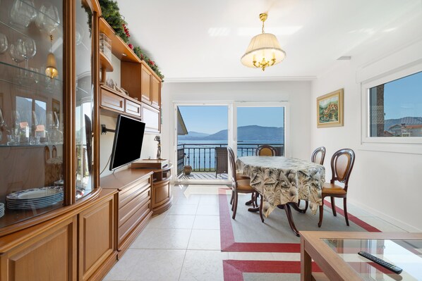A modern kitchen with a dining area, a TV, and a view of the sea.