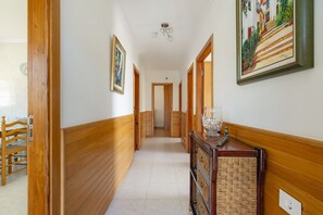 Un couloir aux murs lambrissés, un coin repas avec une table et des chaises en bois, et un escalier menant à un autre niveau.