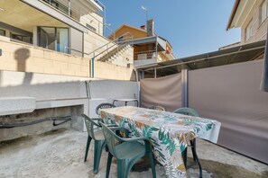 Un patio al aire libre con una mesa y sillas, suelo de hormigón y una vista parcial de un edificio al fondo.