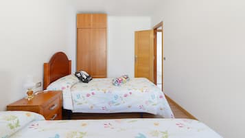Une chambre avec deux lits, une armoire en bois, une table de chevet et une porte donnant sur une autre pièce.