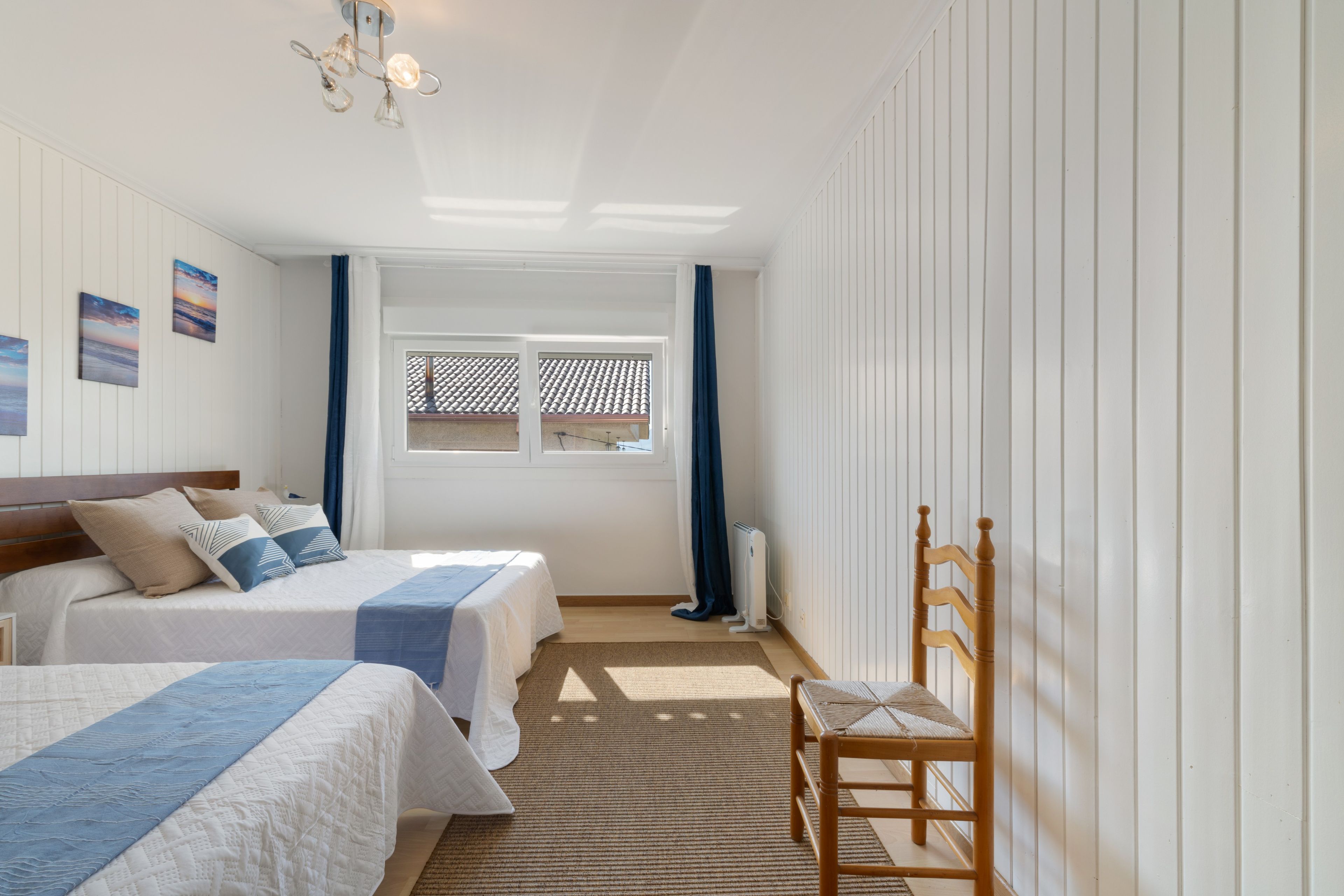 Habitación de hotel con dos camas, una silla de madera, un radiador y una ventana con vistas.