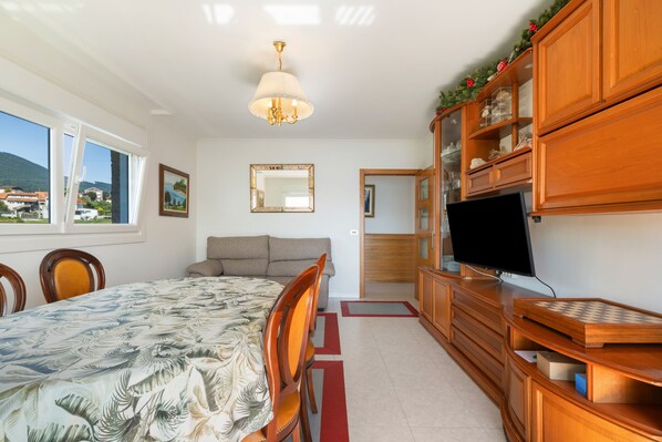 A bedroom with a bed, a television, a wooden cabinet, and a window with a view of houses.