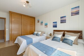 A bedroom with two beds, a wooden wardrobe, a nightstand with a lamp, and wall art.