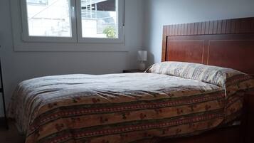 A bedroom with a bed, a nightstand, a lamp, a window, and a wooden headboard.