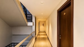 A modern hotel corridor with a wooden door, a staircase, and a fire extinguisher on the wall. - Royal Suites in Marathalli Bangalore (Bengaluru)