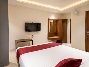 Une chambre d’hôtel avec un lit, un téléviseur fixé au mur, une armoire en bois et une petite table.