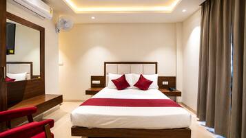 A hotel room with a large bed, a bedside table, a mirror, and a red chair.