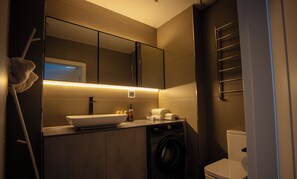 Un baño moderno con lavamanos, espejo, toallero y lavadora.