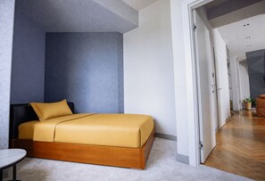 A modern bedroom with a bed, a nightstand, and a door leading to a hallway.
