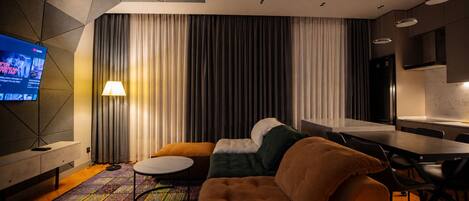 A modern living room with a sofa, a coffee table, a TV, and a kitchen area.