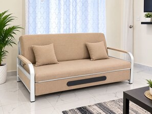 Un sofá color beige con dos cojines, una planta en maceta y un televisor moderno en la pared.