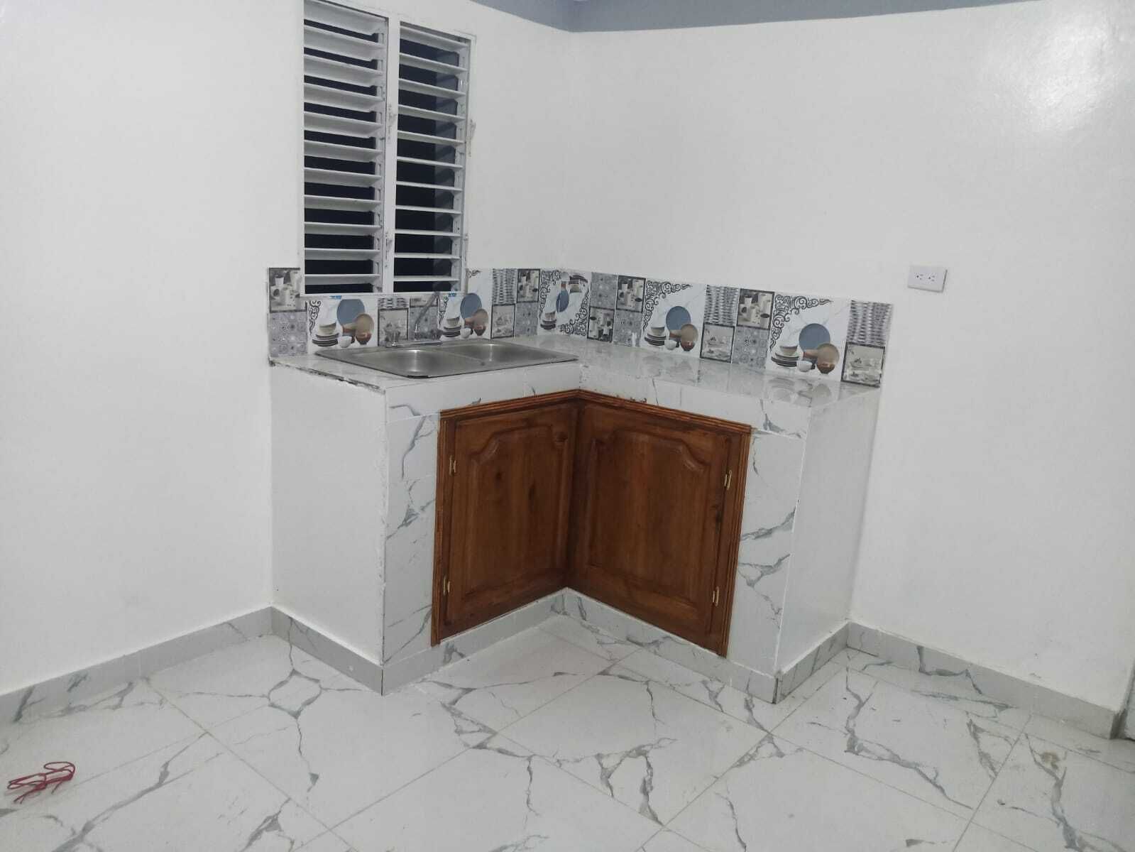 Una cocina con un mueble de esquina, una ventana con persianas y un salpicadero azulejado.