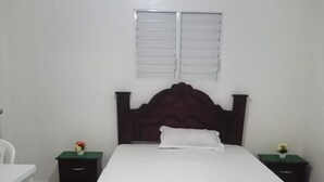 A bedroom with a bed, a nightstand, a chair, a window, and a green mat.