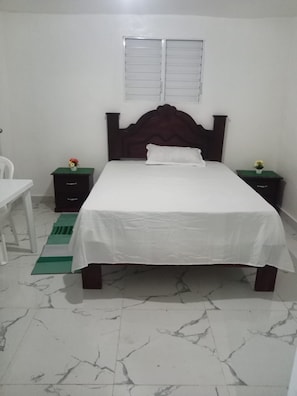 A bedroom with a bed, a nightstand, a chair, a window, and a green mat.