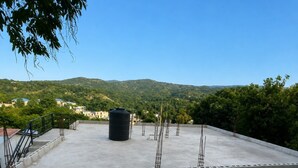 A rooftop terrace with a black water tank, metal poles, and a view of a hilly landscape.