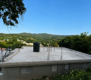A rooftop terrace with a black water tank, metal poles, and a view of a hilly landscape.
