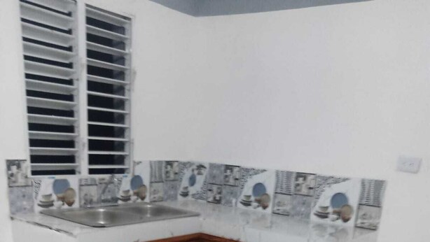 A corner kitchen with white marble tiles, wooden cabinets, and a window with blinds.