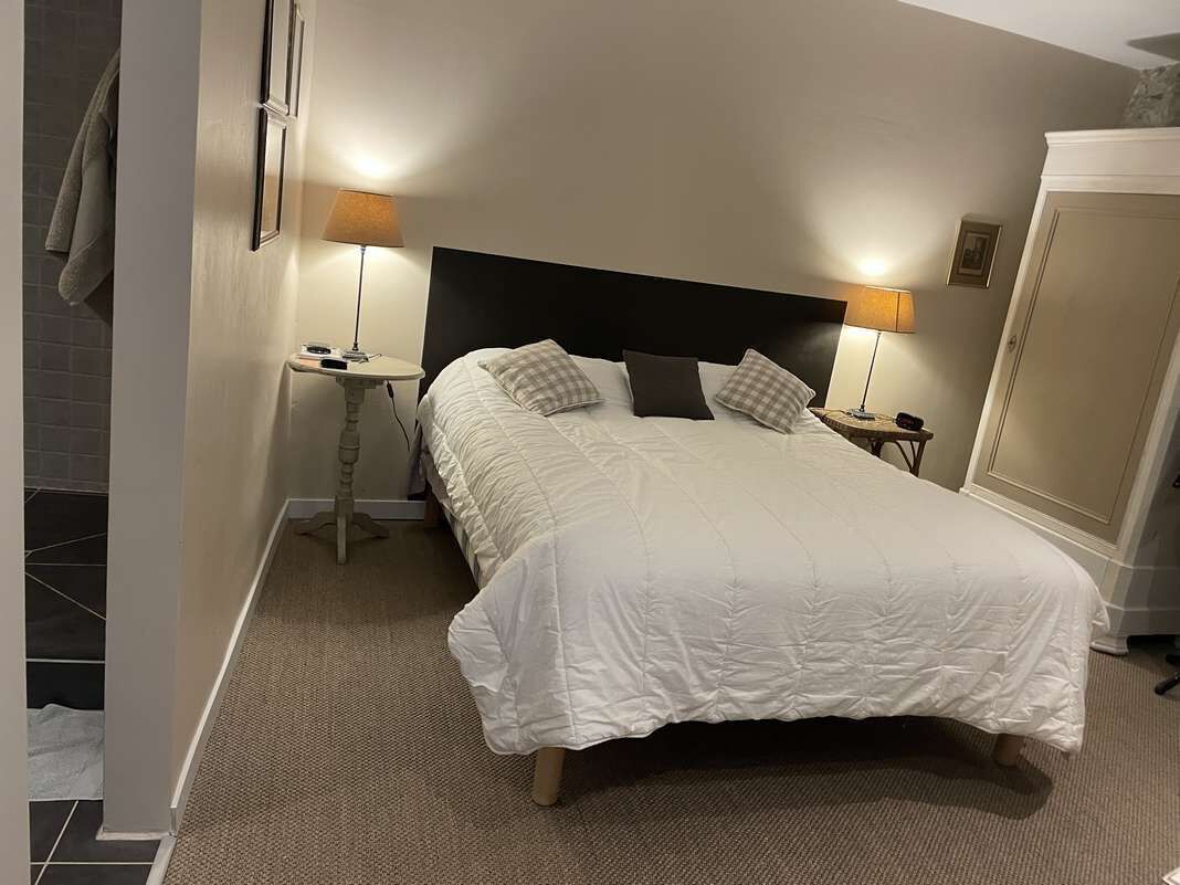 A neatly made bed with a white duvet, two bedside tables with lamps, and a wardrobe in a hotel room.