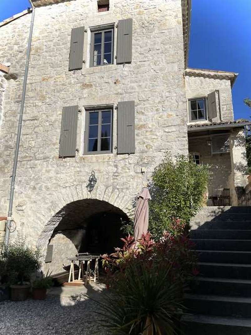 A stone building with a staircase leading to an upper level, a small archway entrance, and a garden area with plants and a table.