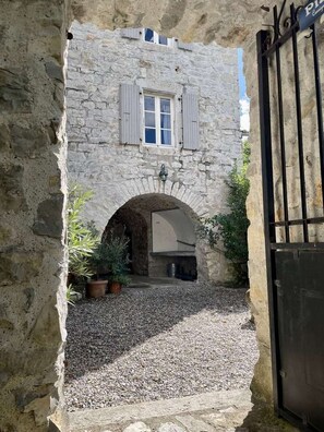 A stone building with a window and shutters, an arched doorway, and a gravel courtyard. - CHARMING, air-conditioned house with a private, fully secured saltwater pool. (Chandolas)