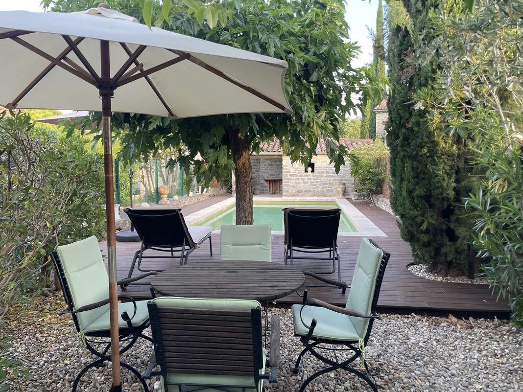 An outdoor patio with a table and chairs, an umbrella, and a stone pathway.