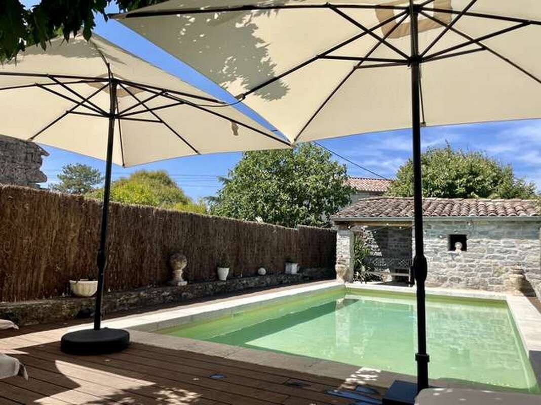 A swimming pool with a wooden deck, surrounded by stone walls and a hedge.