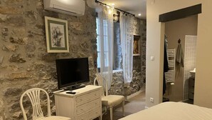 A bedroom with a stone wall, a bed, a TV, a dresser, and a chair. - CHARMING, air-conditioned house with a private, fully secured saltwater pool. (Chandolas)